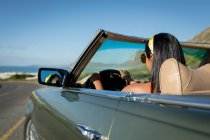 Смешанные гонки женщина за рулем в солнечный день в конвертируемом автомобиле с водительским колесом. Летняя поездка по загородному шоссе у побережья. — стоковое фото