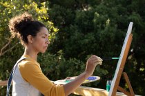 Mulher branca pintando quadro em pé no terraço ensolarado. Ficar em casa em auto-isolamento durante o bloqueio de quarentena. — Fotografia de Stock