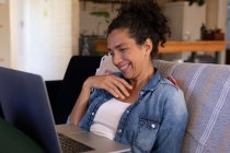 Mulher branca sorrindo usando laptop em chamada de vídeo sentado no sofá em casa. Ficar em casa em auto-isolamento durante o bloqueio de quarentena. — Fotografia de Stock