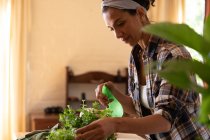 Souriante femme caucasienne arrosant des plantes à la maison. Rester à la maison en isolement personnel pendant le confinement en quarantaine. — Photo de stock