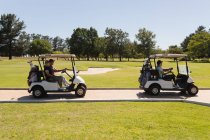 Due coppie anziane caucasiche che guidano golf buggy sul campo da golf parlando e sorridendo. sport di golf hobby, sano stile di vita pensione. — Foto stock