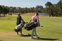 Two caucasian senior man and woman wearing face masks walking across golf course holding golf bags. Golf sports hobby, healthy retirement lifestyle during coronavirus covid 19 pandemic. — Stock Photo