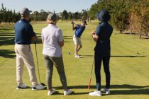 Três homens e mulheres caucasianos a ver um homem a preparar-se para um tiro no verde. passatempo de esportes de golfe, estilo de vida de aposentadoria saudável — Fotografia de Stock
