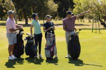 Cuatro hombres y mujeres mayores caucásicos sosteniendo bolsas de golf y hablando. deportes de golf hobby, estilo de vida de jubilación saludable - foto de stock