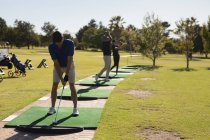 Zwei kaukasische Senioren und eine Frau mit Golfschläger bereiten sich auf den Schlag auf dem Grün vor. Golf-Sport-Hobby, gesunder Lebensstil im Ruhestand. — Stockfoto
