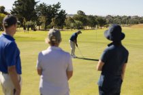 Три кавказькі старші чоловіки і жінки спостерігають, як чоловік бере постріл на зелений. гольф спортивне хобі, здоровий спосіб життя на пенсії — стокове фото