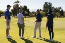 Quatre hommes et femmes âgés caucasiens se préparent à tirer sur le vert. golf passe-temps sportif, mode de vie sain à la retraite — Photo de stock
