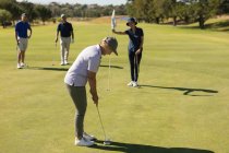 Drei kaukasische ältere Männer und Frauen beobachten den Mann bei der Aufnahme auf dem Grün. Golf-Sport-Hobby, gesunder Lebensstil im Ruhestand — Stockfoto