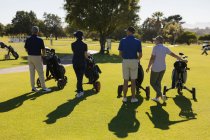 Vier kaukasische Senioren gehen mit Golftaschen über den Golfplatz. Golf-Sport-Hobby, gesunder Lebensstil im Ruhestand — Stockfoto