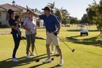 Cuatro hombres y mujeres mayores caucásicos chocan los cinco con palos de golf. Golf deportes hobby, estilo de vida de jubilación saludable - foto de stock