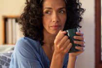 Thoughtful caucasian woman holding green mug sitting on sofa at home. Staying at home in self isolation during quarantine lockdown. — Stock Photo