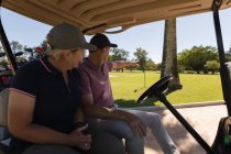 Caucásico hombre y mujer senior conduciendo buggy de golf en el campo de golf hablando y sonriendo. Golf deportes hobby, estilo de vida de jubilación saludable. - foto de stock