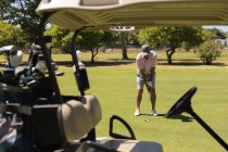 Mulher idosa caucasiana segurando clube de golfe se preparando para tiro no verde pelo saco. Esportes de golfe passatempo, estilo de vida de aposentadoria saudável. — Fotografia de Stock