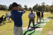 Trois hommes âgés caucasiens et une femme tenant un club de golf se préparent à tirer sur le vert. Golf passe-temps sportif, mode de vie sain à la retraite. — Photo de stock