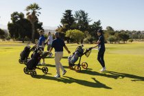 Quatro homens e mulheres caucasianos a atravessar o campo de golfe com sacos de golfe. Esportes de golfe passatempo, estilo de vida de aposentadoria saudável — Fotografia de Stock