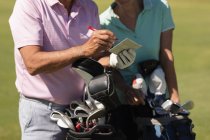 Homem e mulher seniores caucasianos escrevendo pontos em um caderno. Esportes de golfe passatempo, estilo de vida de aposentadoria saudável. — Fotografia de Stock