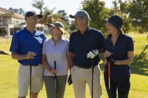 Четыре белых старших мужчины и женщины держат клюшки для гольфа и разговаривают. Спортивное увлечение гольфом, здоровый пенсионный образ жизни — стоковое фото