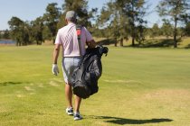 Kaukasischer Senior mit Gesichtsmaske läuft mit Golftasche über den Golfplatz. Golf Sport Hobby, gesunder Lebensstil im Ruhestand während Coronavirus covid 19 Pandemie. — Stockfoto
