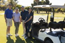 Чотири кавказькі старші чоловіки і жінки, що стоять під гольфом баггі, дивляться на камеру і посміхаються. гольф спортивне хобі, здоровий спосіб життя на пенсії — стокове фото