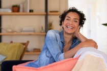 Retrato de mujer caucásica sentada en un sofá y sonriendo a la cámara, relajándose en casa. Permanecer en casa en aislamiento durante el bloqueo de cuarentena. - foto de stock