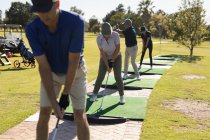 Trois hommes âgés caucasiens et une femme tenant un club de golf se préparent à tirer sur le vert. Golf passe-temps sportif, mode de vie sain à la retraite. — Photo de stock