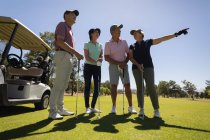Четыре белых старших мужчины и женщины стоят у сумки, держа клюшки для гольфа и разговаривая. гольф-спортивное хобби, здоровый пенсионный образ жизни — стоковое фото