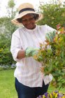 Африканська старша жінка в садівничих рукавицях посміхається під час садівництва в саду. Залишайтеся на самоті в карантинній камері. — стокове фото