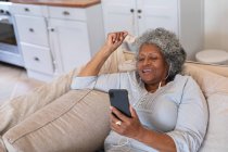 Femme âgée afro-américaine souriant tout en ayant un appel vidéo sur smartphone à la maison. rester à la maison en isolement personnel en quarantaine — Photo de stock