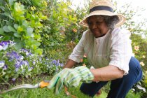 Donna anziana afroamericana che indossa guanti da giardinaggio sorridente mentre fa giardinaggio in giardino. rimanere in isolamento in isolamento in quarantena — Foto stock