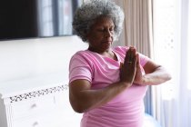 Mujer mayor afroamericana practicando yoga y meditando en casa. permaneciendo en casa en aislamiento en cuarentena - foto de stock