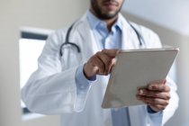 Médico masculino de raza mixta usando tableta digital. Protección sanitaria higiénica durante la pandemia del coronavirus covid 19. - foto de stock