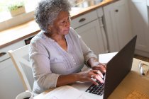 Pensativo afroamericano anciano mujer usando el ordenador portátil en casa. permaneciendo en casa en aislamiento en cuarentena - foto de stock