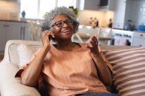 Femme âgée afro-américaine souriant tout en parlant sur smartphone à la maison. rester à la maison en isolement personnel en quarantaine — Photo de stock