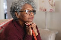 Close up of thoughtful african american senior woman holding walking stick at home. staying at home in self isolation in quarantine lockdown — Stock Photo