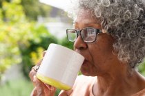 Primo piano di una donna anziana afro-americana premurosa che tiene in mano una tazza di caffe 'mentre e' seduta sul portico. rimanere in isolamento in isolamento in quarantena — Foto stock