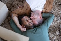 Multi ethnic gay male couple lying on the floor and embracing at home. enjoying time staying at home in self isolation during quarantine lockdown. — Stock Photo
