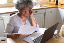 Femme âgée afro-américaine stressée utilisant un ordinateur portable et calculant les finances à la maison. rester à la maison en isolement personnel en quarantaine — Photo de stock