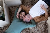 Couple masculin gay multi ethnique couché sur le sol et embrassant à la maison. profiter du temps passé à la maison en isolement personnel pendant le confinement en quarantaine. — Photo de stock