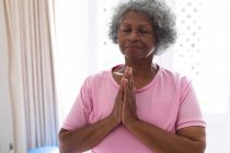 Mujer mayor afroamericana practicando yoga y meditando en casa. permaneciendo en casa en aislamiento en cuarentena - foto de stock