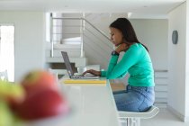 Mujer afroamericana usando portátil mientras trabaja desde casa. permaneciendo en casa en aislamiento en cuarentena - foto de stock