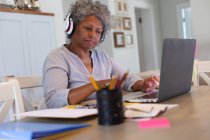 Mulher idosa afro-americana cuidadosa usando fones de ouvido usando laptop em casa. ficar em casa em auto-isolamento em quarentena — Fotografia de Stock