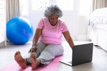 Afrikanische Seniorin benutzt Laptop, während sie zu Hause Yoga praktiziert. Zu Hause bleiben in Selbstisolierung in Quarantäne — Stockfoto