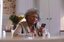 Африканская старшая женщина использует смартфон дома. оставаться дома в изоляции в карантинной изоляции — стоковое фото