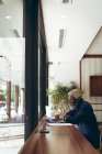 Homme aîné afro-américain assis à table dans un café travaillant avec un ordinateur portable et souriant. nomade numérique dans la ville. — Photo de stock