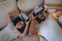 Homme afro-américain et sa fille couchés dans le salon en utilisant un casque vr. rester à la maison en isolement personnel pendant le confinement en quarantaine. — Photo de stock