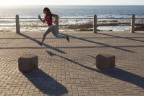 Donna afroamericana concentrata, che si allena su una passeggiata in riva al mare correndo. Fitness stile di vita sano all'aperto. — Foto stock