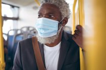 African american senior man wearing face mask standing on bus. digital nomad out and about in the city during coronavirus covid 19 pandemic. — Stock Photo