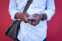 Sezione centrale dell'uomo in piedi contro muro rosso in strada utilizzando smartphone. nomade digitale in giro per la città. — Foto stock