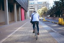 Vista posteriore dell'uomo anziano afroamericano in bicicletta per strada. nomade digitale in giro per la città. — Foto stock