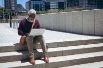 Afro-americano idoso sentado em degraus na rua usando laptop. nômade digital para fora e sobre na cidade. — Fotografia de Stock